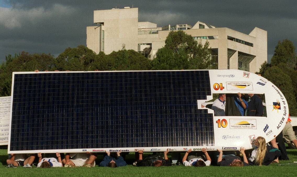 The ACTEW Spirit of Canberra, having run out of battery power, is "energised" outside Questacon. Not having their special support trailer on location, crew members laid on the grass and held the solar cell roof upright to catch the fading sunlight.  Photo: Graham Tidy