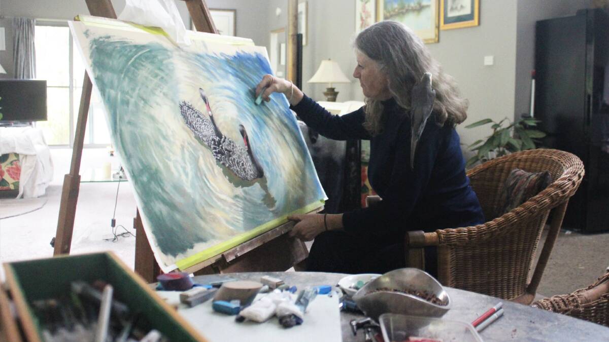 Moruya's Debra Smith with her cockatiel Phoenix on her shoulder as she works on a pastel piece for the upcoming exhibition.