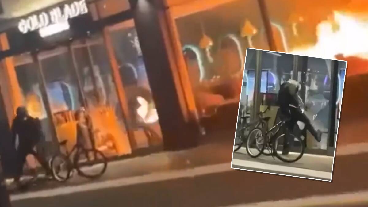 A masked bike rider is seen to break the glass entrance of the Gungahlin business before lighting it on fire. Pictures Reddit
