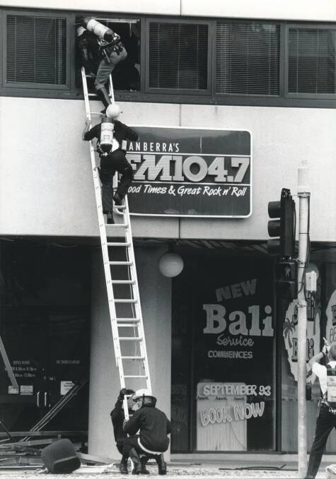 Firefighters climb a ladder into the Jolimont Centre to check if anyone was still inside, as police with revolvers drawn provide protection. Picture by Graham Tidy