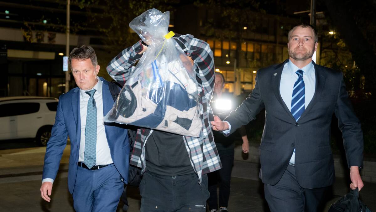 Steve Fabriczy holds up a bundle of clothes in an attempt to shield his identity as he is led into City Station on Thursday night. Picture by Elesa Kurtz