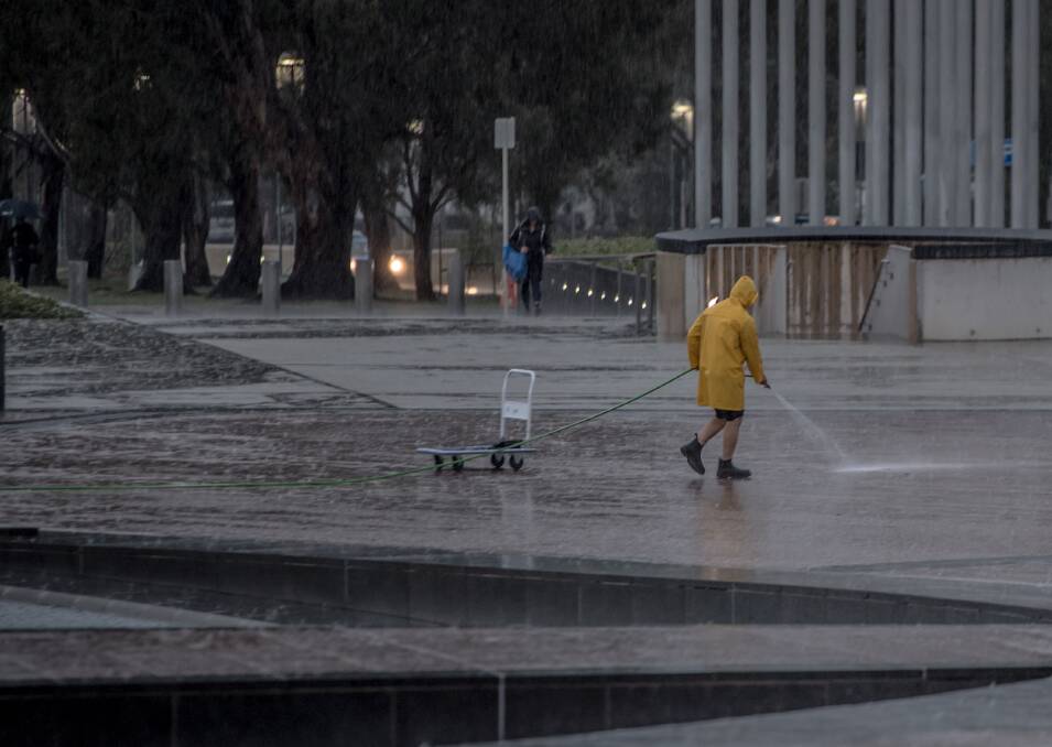 A worker hoses the concrete at the front of Parliament house in the rain. Picture: Karleen Minney